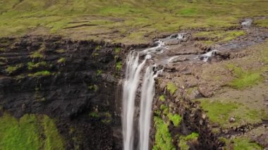 Uçurumdan düşen sersemletici şelalenin havadan görünüşü. Faroe Adaları 'ndaki Gasadalur Köyü yakınlarında Mulafossur şelalesi. İleriye dönük çekim, gün ışığı, bulutlu hava