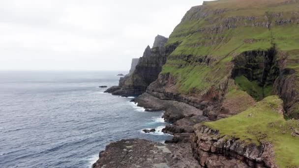 Vista aérea trasera de enormes acantilados en las islas Feroe, montaña rocosa verde, potentes olas oceánicas, en un día nublado de verano, prado verde y roca en la naturaleza salvaje, salvaje sin casa. — Vídeo de stock