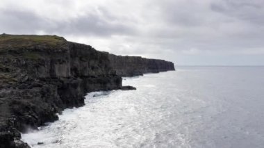 Hava manzaralı yüksek kaya kayalıkları, okyanus dalgaları kayalıklara çarpıyor. Okyanusun gücü, güçlü dalgalar köpük yaratıyor, vahşi doğa, vahşi yaşam, vahşi insanlar yok, gökyüzünde bulutlar, manzaralar