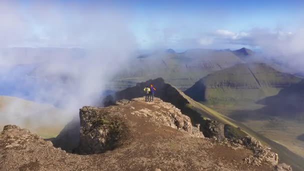Вид с воздуха на двух человек на вершине горы с видом на красивый пейзаж, море, скалу, гору, скалу, обертывание облаками — стоковое видео