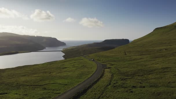 Carro dirigindo ao longo da vista para a estrada costeira na ilha verde selvagem ao pôr do sol.Cinematic visão traseira approaching.Faroe Island estrada ao longo da bela costa. Ilha Faroé, Dinamarca. Voo aéreo avançado — Vídeo de Stock