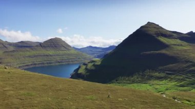 Çimlerin üzerinde uçan dron uçurum ve mavi denizin üzerinde. Dağın bodrumundaki köy. Güneşli bir yaz gününde, arka plandaki dağ ve uçurumda.