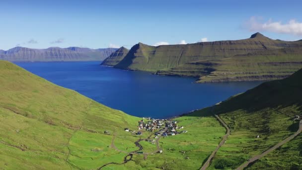 Drone che vola sopra erba coperto scogliera e mare blu. Villaggio nel seminterrato della montagna. Sullo sfondo montagna e scogliera in una giornata di sole estivo. — Video Stock