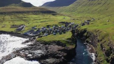 Denizin üzerinde uçan insansız hava aracı, yeşil çimlerle kaplı devasa ve görkemli bir uçurum çerçevesi. Güneşli bir yaz gününde uçurumun bodrumunda küçük bir köy.