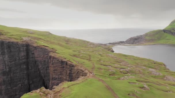 Μέρος μιας σειράς, εναέρια άποψη του διάσημου βράχου στα νησιά Φερόε. Πτήση πάνω από το πράσινο γρασίδι και χωματόδρομο του βράχου σε μια συννεφιασμένη ημέρα. Ακτή στο παρασκήνιο — Αρχείο Βίντεο