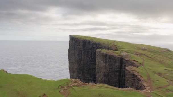 Onderdeel van een serie, luchtfoto 's van de beroemde klif op de Faeröer. Vlucht over groen gras en onverharde weg van de klif in een bewolkte dag. — Stockvideo