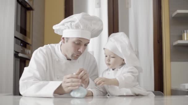 Papá e hijo lanzando pasta de azúcar azul en su cocina casera. Momentos de padre e hijo mientras cocinan. Padre enseñando a hijo a cocinar un pastel en casa. — Vídeo de stock