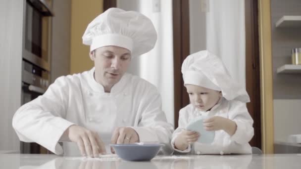 Тато з сином викручують синю цукрову пасту на своїй домашній кухні. Моменти батька і сина під час приготування їжі. Батько навчає сина готувати вдома торт.. — стокове відео