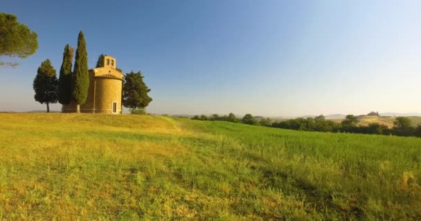 Aerial view of colored countryside in Tuscany. Sun goes down at horizon.Blue sky, green hill, agricultural field and abandoned church with off road trip. — Stock Video