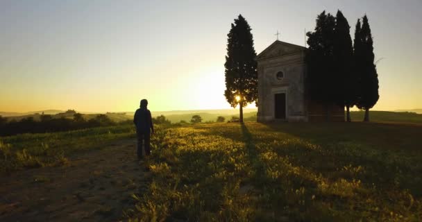 Igreja abandonada na Toscana durante o pôr do sol. Luz do sol dourada brilhando no campo. Homem caminhando e admirando paisagem — Vídeo de Stock