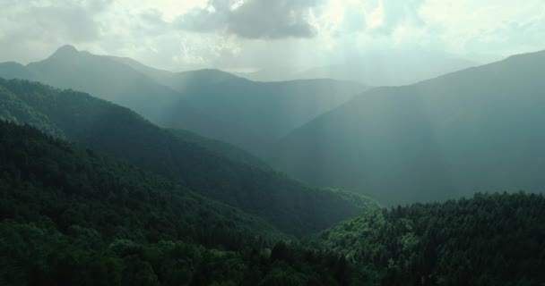Aerial view of pristine green mountain in summer. Sunlight cross over clouds. Foggy mountain range in background. slow motion — Stock Video