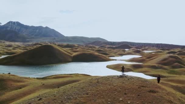 Twee mensen in een surrealistisch landschap. Gebogen rivier stak woestijnheuvel over. Bergketen op de achtergrond. — Stockvideo