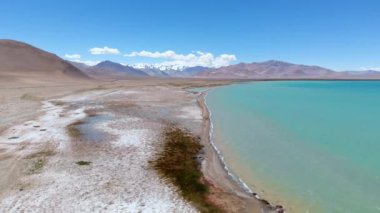 Tacikistan 'daki renkli göl manzarası, güneşli bir günde arka planda dağ aralığı. Mavi ve kristalize gölü gösteren hava manzarası. Beyaz bulutlu mavi gökyüzü.