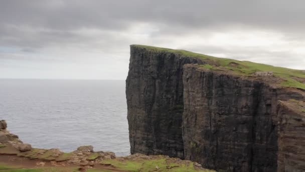 Часть серии, воздушный вид знаменитой скалы на Фарерских островах. Полет над зеленой травой и грунтовой дорогой скалы в облачный день. — стоковое видео