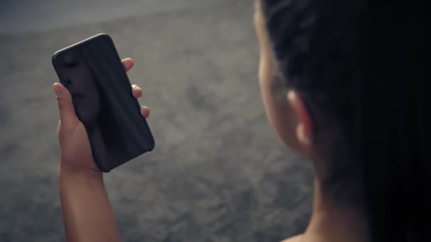 Back view of fitness woman using smart phone at home. Woman preparing for workout using smart phone.Woman doing a tap on mobile phone while resting during fitness training — Stock Video