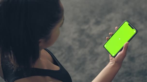 Back view of fitness woman using green screen smart phone at home. Woman preparing for workout using smart phone.Woman using mobile phone while resting during fitness training — Stock Video