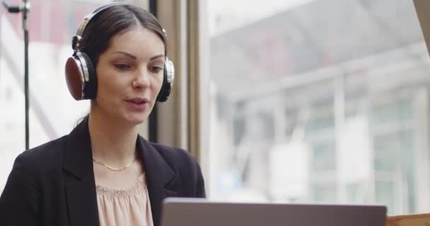 Nahaufnahme Porträt einer erwachsenen kaukasischen Geschäftsfrau mit Kopfhörern vor dem Laptop bei einer Videokonferenz in einem Café. Fernarbeit in einer Bar für eine junge Frau im Freizeitanzug. — Stockvideo