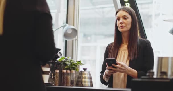 Kund kvinna betalar med NFC-teknik med telefon och kreditkort, kontaktlös betalning med student girl.Pay via telefon på elektronisk betalningsmaskin eller kortläsare. E-pengar i kontantlös plånbok — Stockvideo