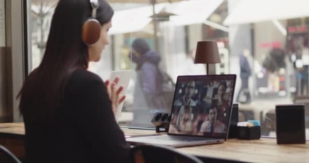 Achteraanzicht van een blanke vrouw die werkt aan een nieuw project in een coffeeshop. Vrouw in slim casual pak spreekt met collega 's tijdens een webconferentie, luisterend met een koptelefoon. Werk op afstand. — Stockvideo