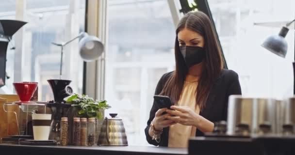 Klantvrouw in medische bescherming masker betalen met behulp van NFC-technologie met telefoon en creditcard, contactloze betaling met student meisje.Betalen per telefoon op elektronische betaalmachine of kaartlezer. — Stockvideo