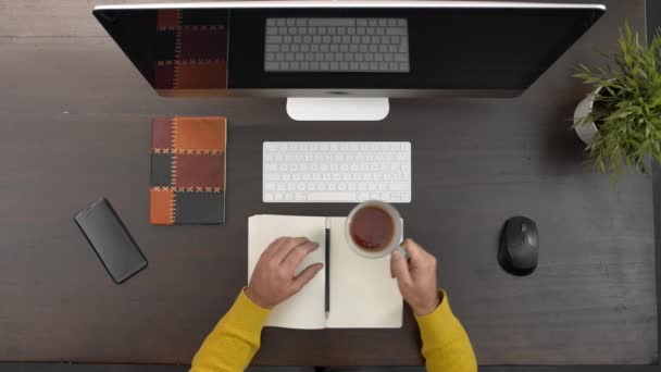 Zbliżenie człowieka słuchającego konferencji na komputerze, pijącego herbatę w miejscu pracy.Przed człowiekiem notatnik ołówkowy i smartfon. Czysty i precyzyjny człowiek. — Wideo stockowe