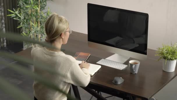 Mujer mirando monitores ordenador, escuchando conferencia, lección, escribiendo y tomando notas. Mujer moviendo su cabello en un lado — Vídeos de Stock