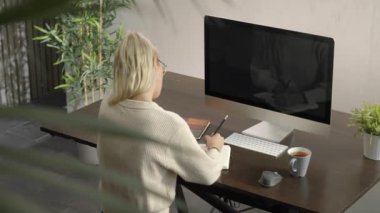 Kadın öğrenci evde monitörlere bakıyor, uzaktan konferans ya da ders dinliyor, yazıyor ve not alıyor. Evde uzaklık öğrenimi.