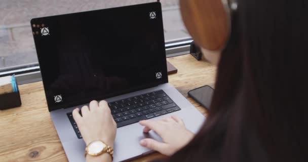Πίσω όψη καυκάσιας γυναίκας που δουλεύει με λάπτοπ σε καφετέρια. Γυναίκα σε smart casual κοστούμι γράφοντας στο laptop κατά τη διάρκεια μιας διάσκεψης web, ακούγοντας με ακουστικά. Απομακρυσμένες θέσεις εργασίας. — Αρχείο Βίντεο