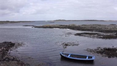 Dalgaların alçak deniz manzarası. Kayalardan ve yosunlardan oluşan alçak sularda mavi bir tekne. Düşük gelgitte İrlanda kıyı şeridine insansız hava aracı bakış açısı