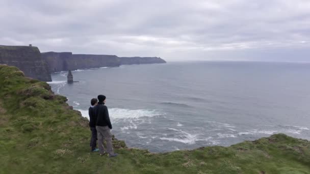 Luchtfoto van prachtige Ierse kliffen van moeder, jong stel kijken naar het landschap, panorama. Bewolkte lucht op de achtergrond, ruwe zee. Beroemde plaats in Ierland, moeder van de kliffen — Stockvideo
