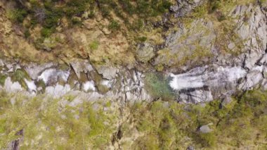 Dağdaki kayalıklardan akan şelale manzarası. Her iki tarafta yeşil orman