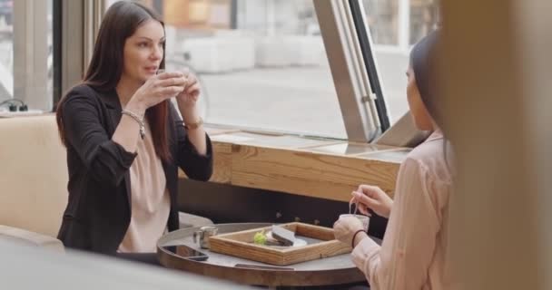 两个成年女商人坐在酒吧里聊天的倒影 在咖啡馆里吃早饭时 两个多元文化的朋友正在吃饭 微笑和大笑 高质量的4K镜头 — 图库视频影像