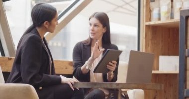 Modern ve endüstriyel bir kafede oturan ve çalışan iki kadın. Laptop ve tablet üzerinde çalışan iki çok ırklı meslektaşım konuşuyor. Takım çalışması, şirket, çeşitlilik ve sosyal konsept .k