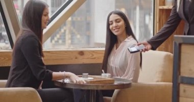 Temassız NFC Ödeme Teknolojisi ile Smartphone 'da oturan Kadın Müşteri Ödemeleri. Müşteri banka terminali üzerinden ödeme yapmak için cep telefonu kullanıyor. Bardaki arkadaşlar konuşur, öder ve giderler. 4k görüntü