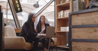 Modern ve endüstriyel bir kafede oturan ve çalışan iki kadın. Laptop ve tablet üzerinde çalışan iki çok ırklı meslektaşım konuşuyor. Takım çalışması, şirket, çeşitlilik ve sosyal konsept .k
