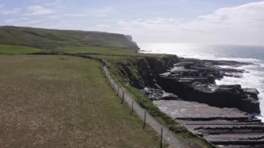 Yeşil tarlaların havadan görünüşü, çayır antenleri: yol, arka planda araba yok. Irelands tepeleri, tarlalar, ufuktaki bulutlar. Rüzgar ve dalgalarla hareket eden deniz. Yüksek kalite 4k görüntü