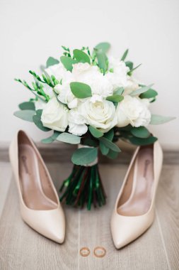 Bir çift zarif ve şık gelinlik ayakkabısı, alyansları, bir buket gülleri ve diğer çiçekleri var.