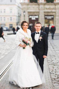 Düğün fotoğrafı çekimi. Gelin ve damat şehirde yürüyorlar. Birbirlerine sarılıp bakan evli bir çift. Tutma buketi