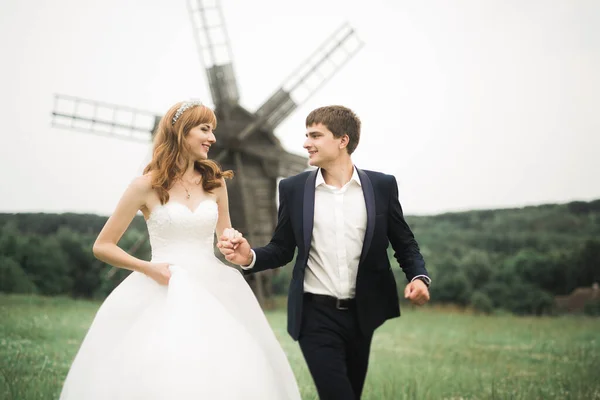 Elegante coppia di sposi felici che passeggiano nel parco il giorno del loro matrimonio con bouquet — Foto Stock