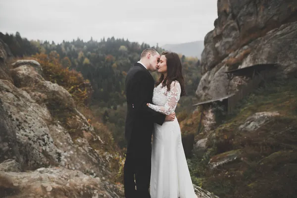 山の岩の上に屋外で結婚式の日に幸せな美しい結婚式のカップルの花嫁と新郎。自然の中で幸せな結婚カップル屋外,柔らかい日当たりの良い光 — ストック写真