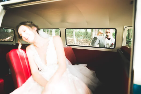 Stylish wedding couple, bride, groom kissing and hugging on retro car.