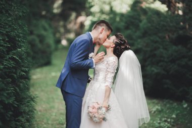 Şık bir çift yeni evliler düğün günlerinde ellerinde buketle parkta yürüyorlar..