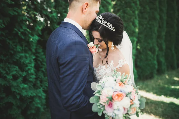 Stylish couple of happy stylish newlyweds walking in the park on their wedding day with bouquet.