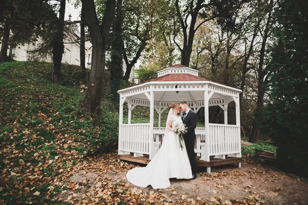 Stylish couple of happy stylish newlyweds walking in the park on their wedding day with bouquet.