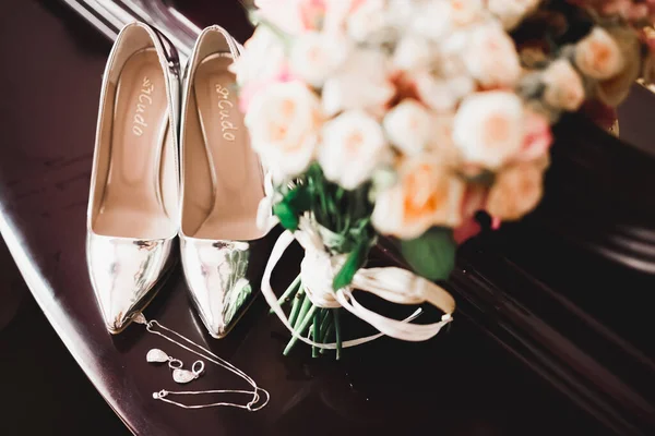 Brides wedding shoes and costume jewellery with roses and other flowers.