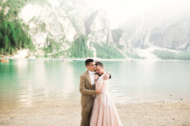 Doğadaki düğün çifti, dağlardaki güzel bir gölün yanında birbirlerine sarılıyorlar beyaz elbiseli güzel model kız. Takım elbiseli adam.