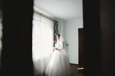 Cüppeli muhteşem gelin bir odada düğün töreni için poz veriyor ve hazırlanıyor..