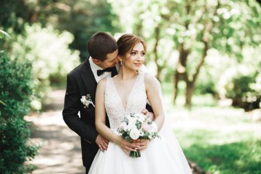 Romantik, peri masalı, mutlu yeni evli çift parkta sarılıp öpüşüyor, arka planda ağaçlar....