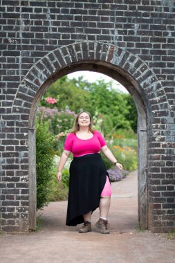 Plus size woman wearing pink and standing in an arch way while on a travel adventure