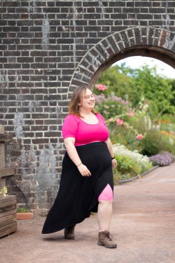 Plus size woman wearing pink and walking around in front of an arch
